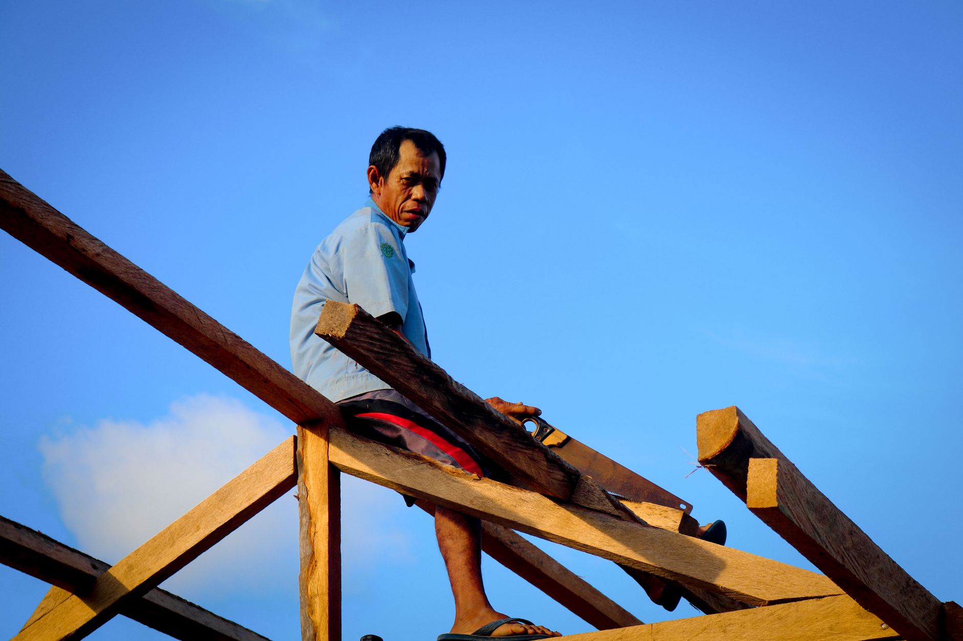 Carpenter skillfully installing roof shingles on residential roofline under bright blue sky