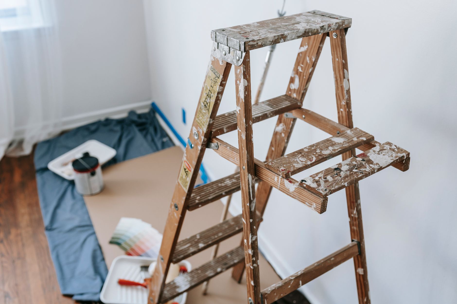 Ladder positioned against house wall with maintenance tools and supplies staged for roof work.